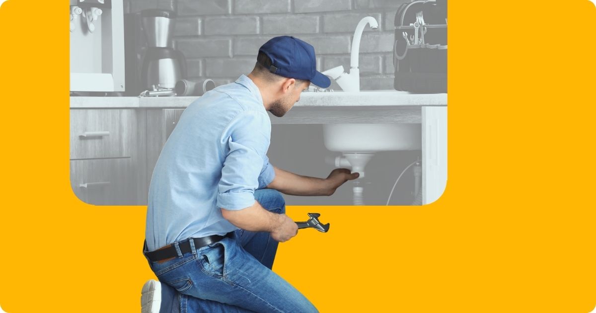 A kneeling plumber works on a sink in the kitchen.