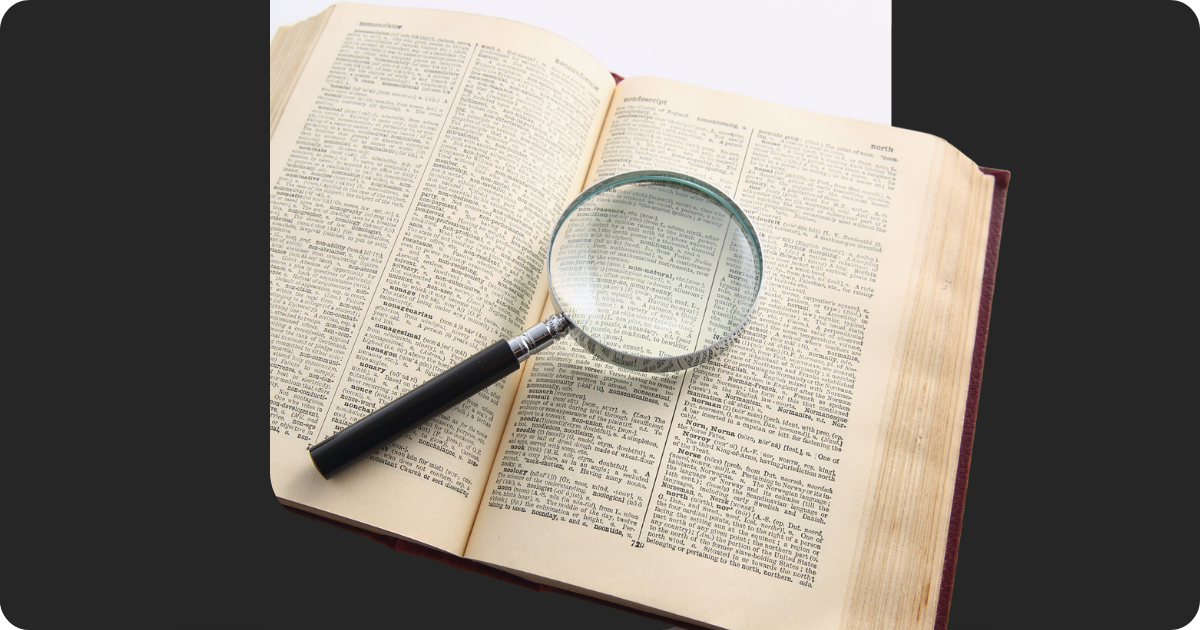 An open dictionary with a magnifying glass laying on the right page.